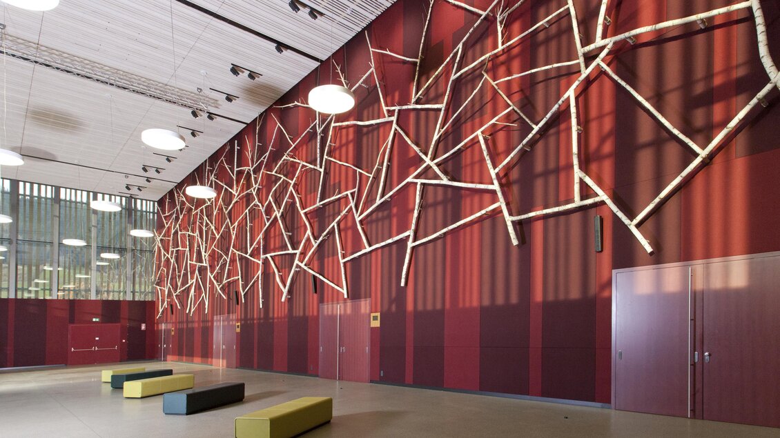 Ein moderner Innenraum mit einer auffälligen Wanddekoration aus Ästen. Bunte Bänke laden zum Verweilen ein. | © Harald Steiner