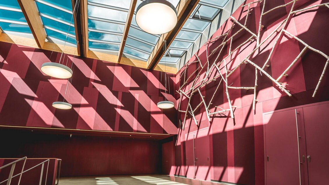 Ein moderner Innenraum mit roten Wänden und großen Fenstern. Das Licht erzeugt interessante Schattenmuster auf dem Boden. | © congress Schladming