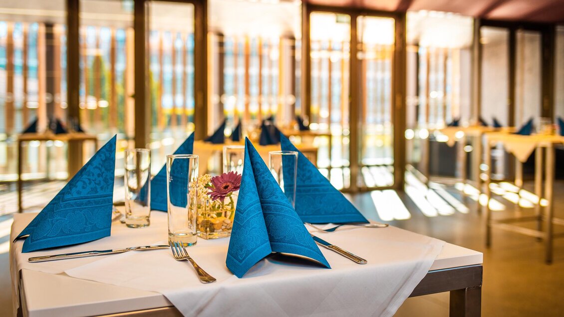 Ein elegantes Restaurant mit einem gedeckten Tisch. Die blauen Servietten und das moderne Ambiente schaffen eine einladende Atmosphäre. | © congress Schladming