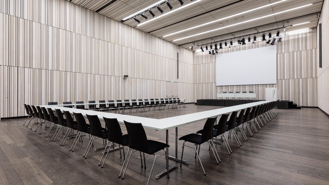 Ein moderner Konferenzraum mit einem großen Tisch in U-Form und vielen Stühlen. Die Wände sind in hellen Farbtönen mit Holzvertäfelung gestaltet. | © Harald Steiner 