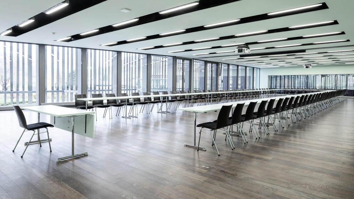 Ein großer, heller Konferenzraum mit langen Tischen und schwarzen Stühlen. Große Fenster sorgen für viel Tageslicht. | © Harald Steiner 