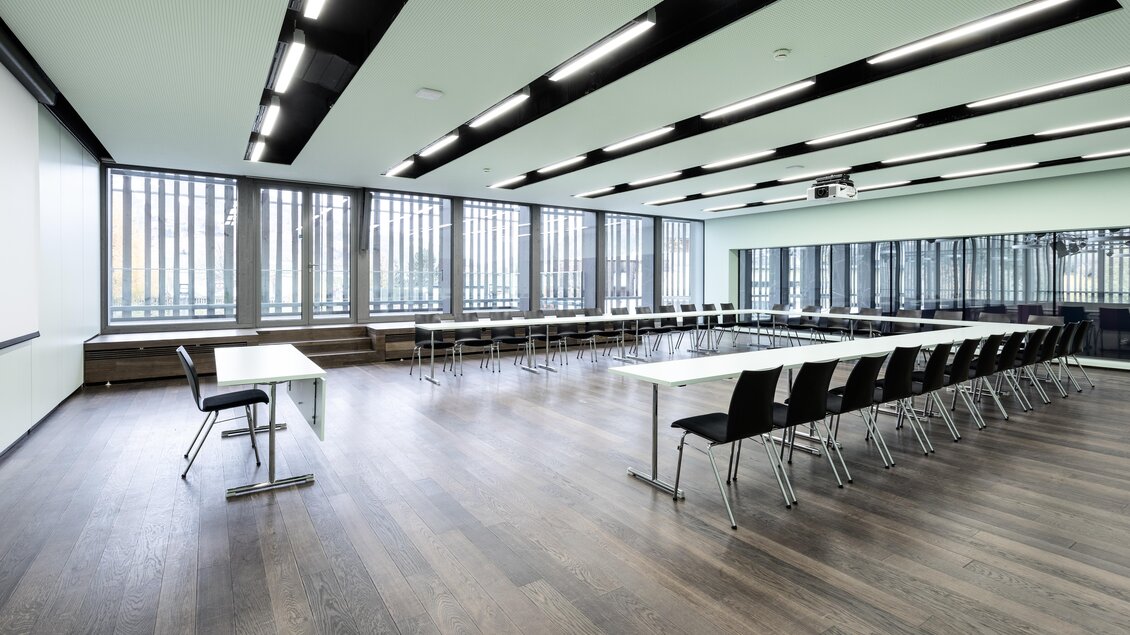 Ein modernes Konferenzzimmer mit großen Fenstern und hellen Wänden. Es sind Tische und Stühle in einem aufgeräumten Raum angeordnet. | © Harald Steiner 
