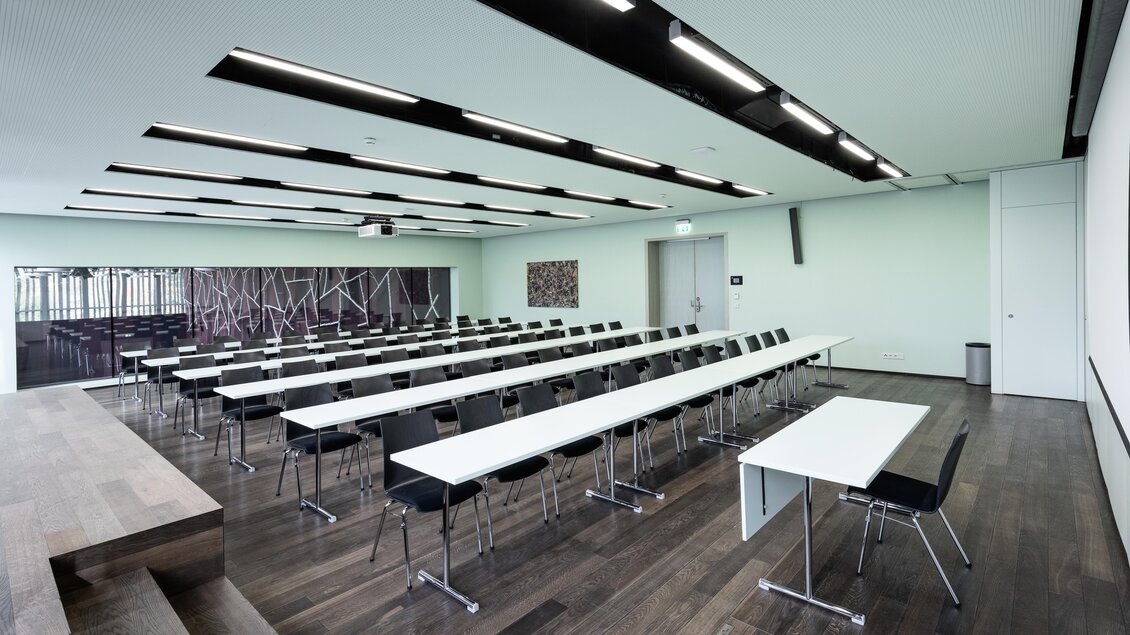Ein moderner Seminarraum mit langen Tischen und Stühlen. Die Wände sind hellgrün und die Beleuchtung ist elegant gestaltet. | © Harald Steiner 