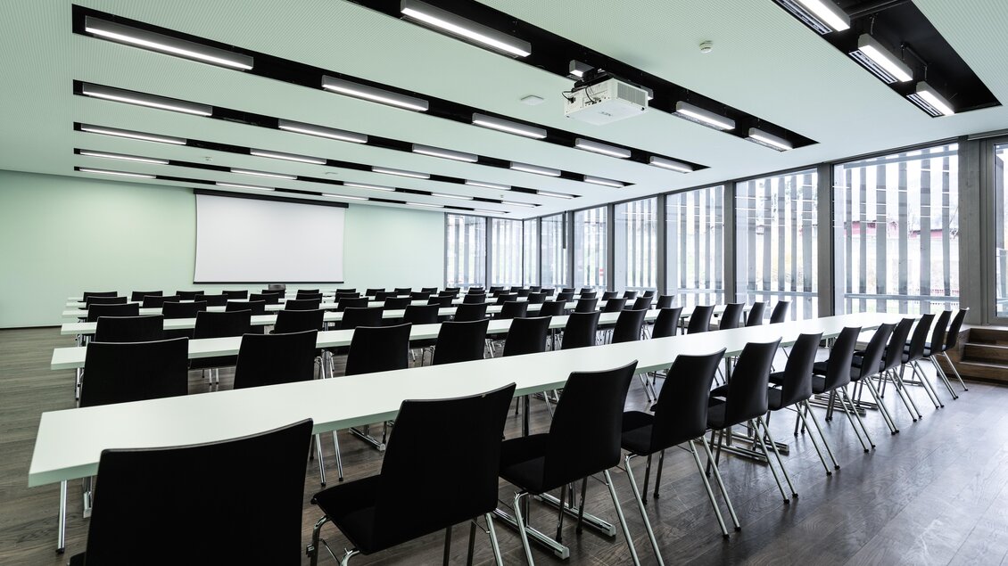Ein moderner Konferenzraum mit langen Tischen und schwarzen Stühlen. Große Fenster lassen viel Licht herein und bieten einen Blick auf die Außenwelt. | © Harald Steiner 