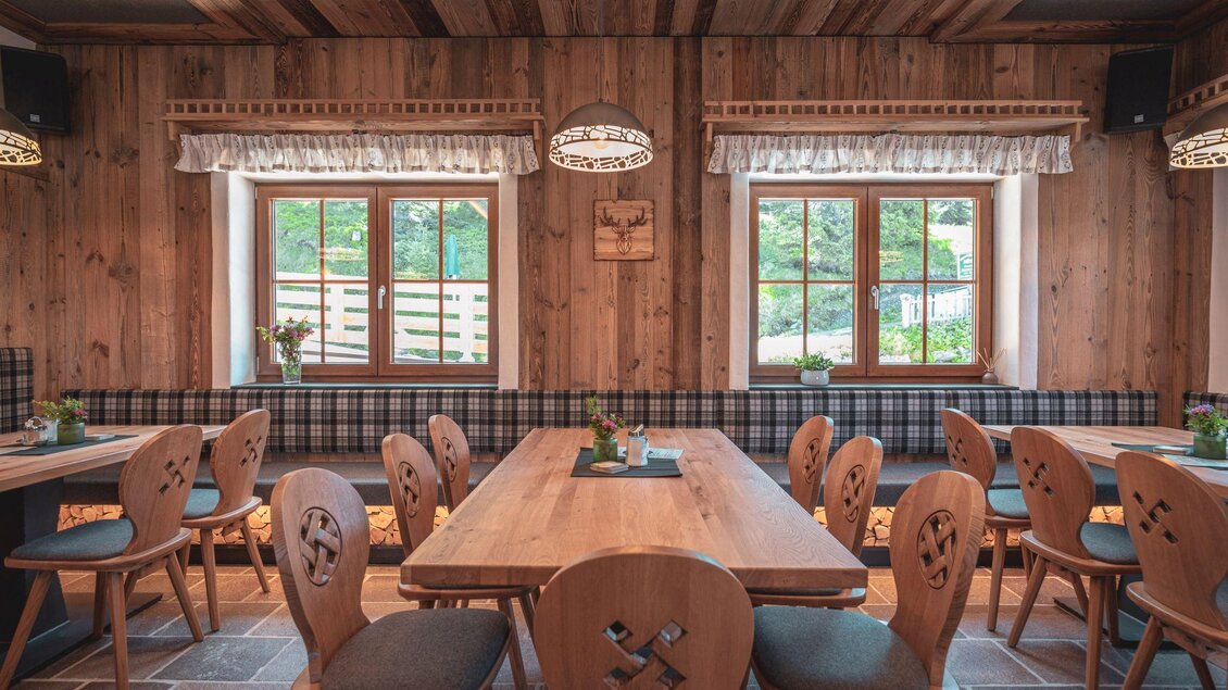 Ein gemütlicher Raum mit Holzstuhl und großen Fenstern. Die Wände sind aus Holz, und die Tische sind sorgfältig gedeckt. | © d´Genussalm