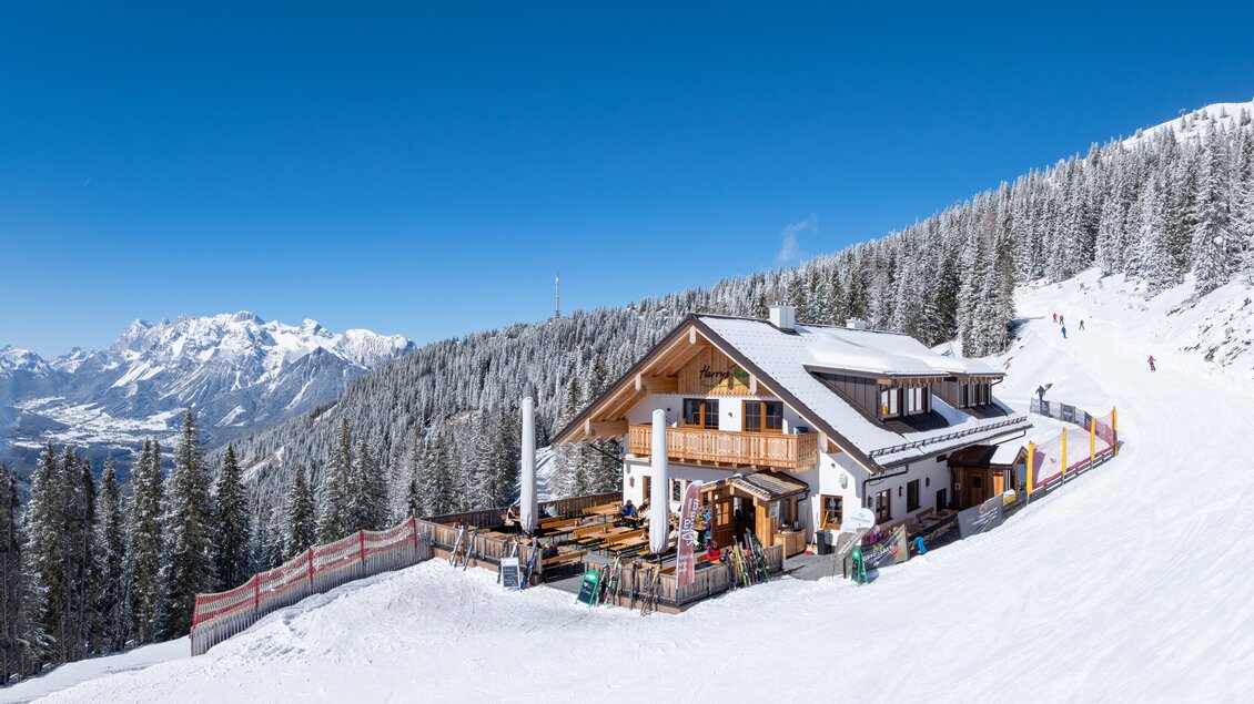 Gemütliche Skihütte mit großer Sonnenterrasse und Skiständern, direkt an der Piste gelegen, mit weitem Blick ins Tal und auf die Bergwelt. | © d´Genussalm