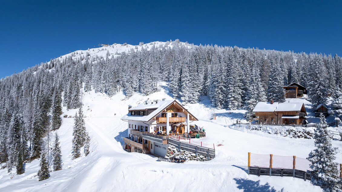 Skihütte Genussalm eingebettet in eine verschneite Waldlandschaft, mit Skipisten und Ausblick auf den Gipfel des Hauser Kaibling. | © d´Genussalm