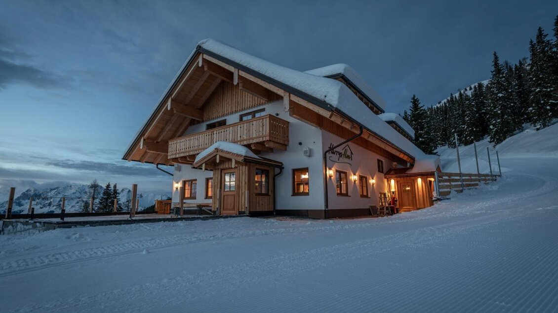 Ein modernes Chalet im Schnee, umgeben von einer winterlichen Landschaft. Der Himmel ist bewölkt und verleiht der Szene eine gemütliche Atmosphäre. | © d´Genussalm