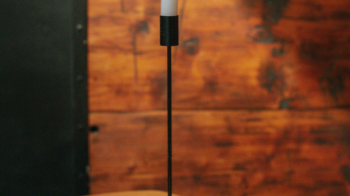 Eine Pizza auf einem Tisch steht neben einer brennenden Kerze. Im Hintergrund sieht man eine rustikale Holzwand. | © Daniela Pattermann