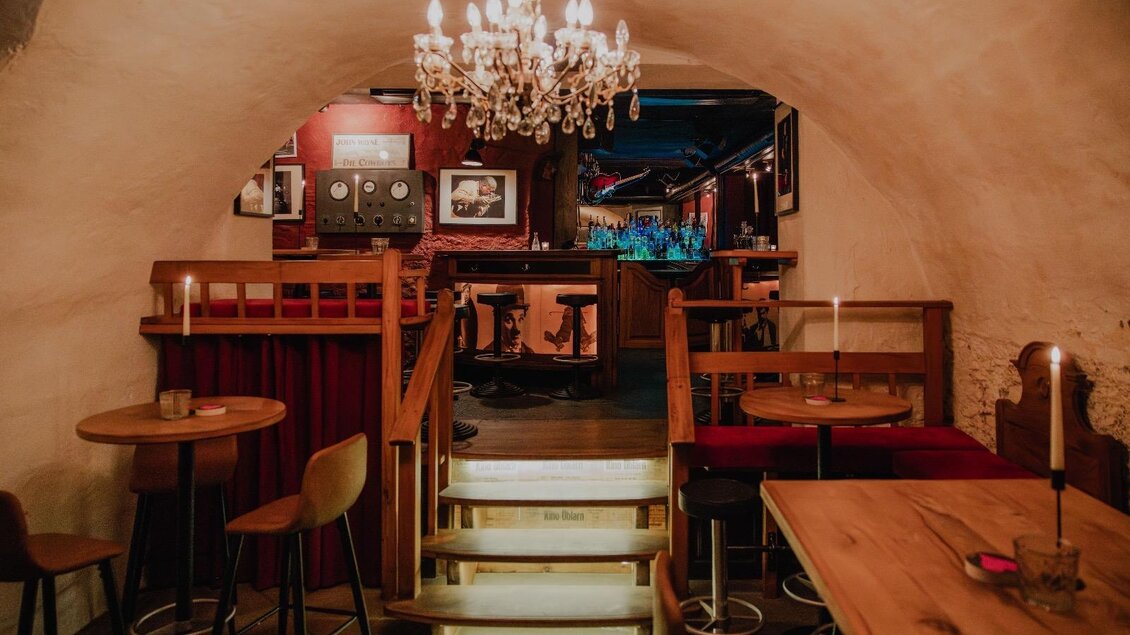 Ein stilvolles Restaurant mit einer gemütlichen Atmosphäre. Im Hintergrund sind eine Bar und ein Kronleuchter zu sehen.